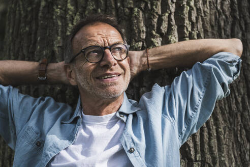 Thoughtful man with hands behind head in front of tree - UUF30809