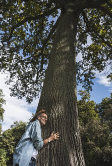 Senior man leaning on tree in park - UUF30813