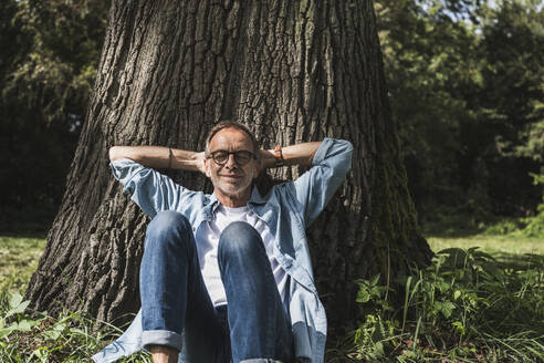 Senior man with hands behind head sitting in park - UUF30816