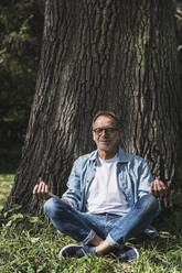 Senior man meditating in lotus position at park - UUF30819