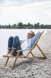 Senior man with coffee cup sitting on deck chair by sea - UUF30829