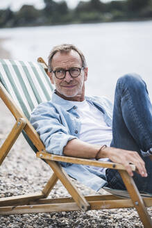 Contemplative man sitting on deck chair at beach - UUF30832