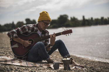 Senior man playing guitar sitting by sea on weekend - UUF30836