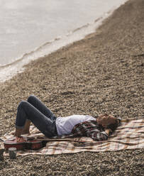 Senior man resting on blanket by sea at beach - UUF30837