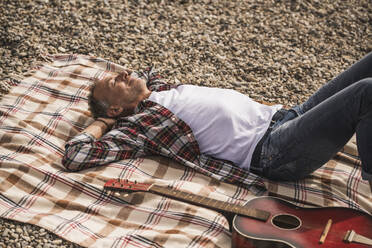 Senior man with eyes closed resting on blanket at beach - UUF30838