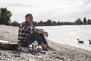 Senior man sitting at beach on weekend - UUF30845