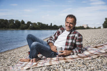 Smiling senior man with coffee cup spending leisure time at beach - UUF30849