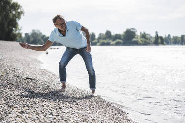 Smiling senior man throwing pebble in sea at beach - UUF30852