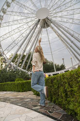 Happy woman gesturing in front of Ferris wheel at amusement park - VPIF08969