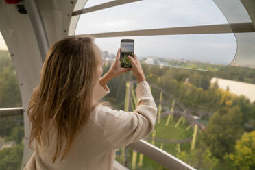 Woman photographing through smart phone and enjoying Ferris wheel ride - VPIF08970