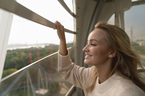 Happy blond woman looking through Ferris wheel window - VPIF08973