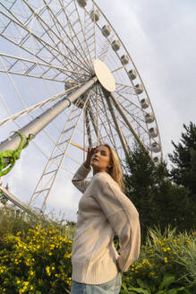 Woman standing in front of Ferris wheel near plants - VPIF08977