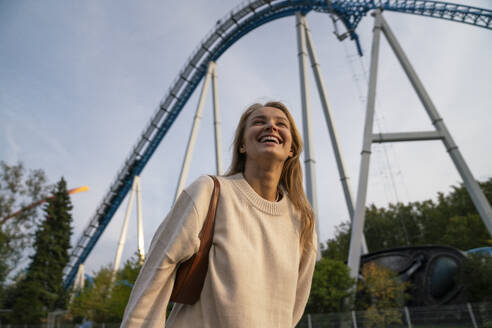 Happy woman laughing and standing in front of rollercoaster - VPIF08979