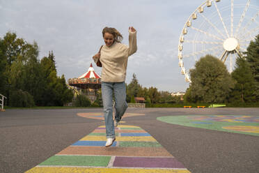 Cheerful woman enjoying and jumping in amusement park - VPIF08980