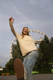Cheerful young woman enjoying in amusement park at sunset - VPIF08983