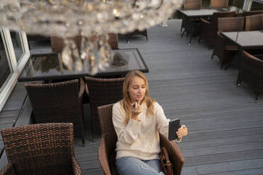 Young woman looking at smart phone and applying lipstick in cafe - VPIF08995