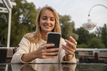 Happy blond young woman using smart phone at table in cafe - VPIF08998