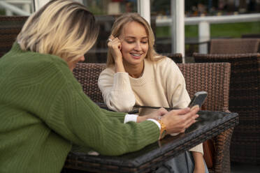 Happy woman with friend using smart phone at table in cafe - VPIF08999