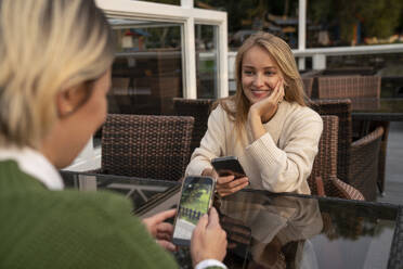 Happy woman with friend looking at photograph on smart phone in cafe - VPIF09000