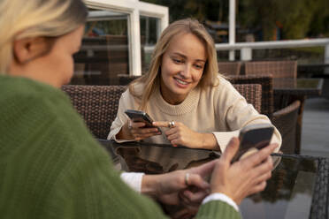 Woman showing smart phone to smiling friend at table in cafe - VPIF09002