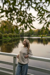 Thoughtful woman leaning on railing in front of lake - VPIF09009