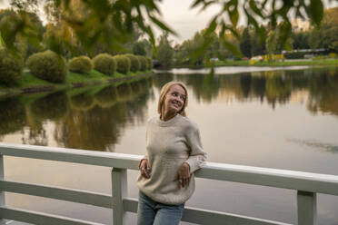 Smiling woman leaning on railing in front of lake at sunset - VPIF09011