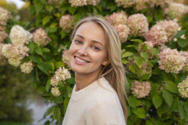 Happy blond woman in front of flowering plant - VPIF09015