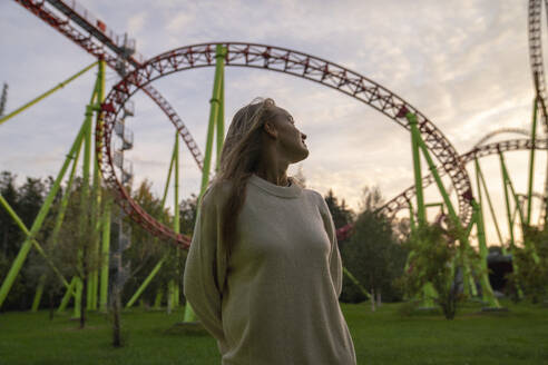 Young woman standing in front of rollercoaster at sunset - VPIF09018