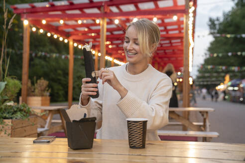 Happy young woman unwrapping food at table in amusement Park - VPIF09027