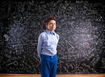 Junge in blauem T-Shirt vor großer Tafel mit mathematischen Symbolen und Formeln - HPIF35405