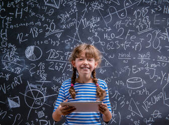 Cute little girl with tablet in front of big blackboard - HPIF35418