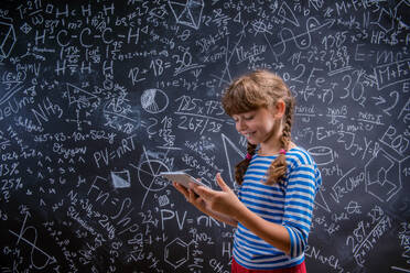 Cute little girl with tablet in front of big blackboard - HPIF35419