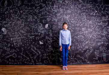 Junge in blauem T-Shirt vor großer Tafel mit mathematischen Symbolen und Formeln - HPIF35443