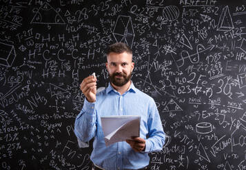 Hipster Lehrer mit Notebook gegen große Tafel mit mathematischen Symbolen und Formeln. Studio Schuss auf schwarzem Hintergrund. - HPIF35521