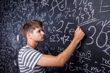 Studentin schreibt auf große Tafel mit mathematischen Symbolen und Formeln, Studioaufnahme auf schwarzem Hintergrund. - HPIF35539