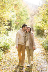 Schönes junges Paar in warmer Kleidung bei einem Spaziergang im Wald, umarmend und küssend. Bunte Herbstnatur. - HPIF35556