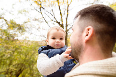 Unbekannter Vater hält seinen Sohn in warmer Kleidung in den Armen bei einem Spaziergang in der bunten Herbstnatur. - HPIF35560