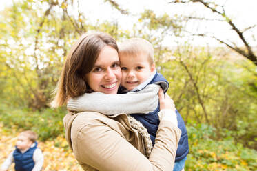 Schöne junge Mutter mit ihren Söhnen in warmer Kleidung auf einem Spaziergang draußen in der bunten Herbstnatur. - HPIF35561