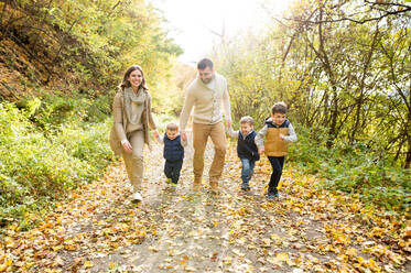 Schöne junge Familie auf einem Spaziergang im Wald. Mutter und Vater mit ihren drei Söhnen in warmer Kleidung draußen in der bunten Herbstnatur. - HPIF35564