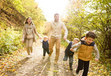 Schöne junge Familie auf einem Spaziergang im Wald, Laufen. Mutter und Vater mit ihren drei Söhnen in warmer Kleidung draußen in der bunten Herbstnatur. - HPIF35565