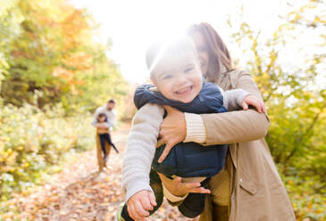 Schöne junge Familie auf einem Spaziergang im Wald. Mutter und Vater mit ihren Söhnen in warmer Kleidung draußen in der bunten Herbstnatur. - HPIF35568