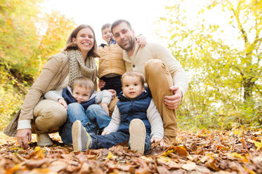 Schöne junge Familie auf einem Spaziergang im Wald. Mutter und Vater mit ihren drei Söhnen in warmer Kleidung draußen in der bunten Herbstnatur. - HPIF35569