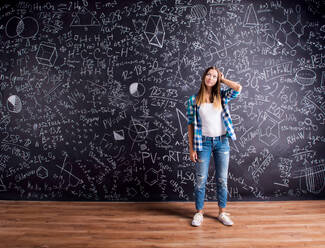 Studentin hält ihren Kopf nachdenklich vor eine große Tafel mit mathematischen Symbolen und Formeln, Studioaufnahme auf schwarzem Hintergrund. - HPIF35582