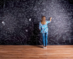 Studentin schreibt auf große Tafel mit mathematischen Symbolen und Formeln, Rückansicht, Studioaufnahme auf schwarzem Hintergrund. - HPIF35583