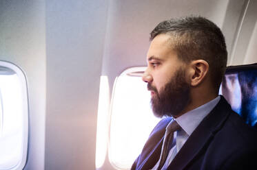 Junger gut aussehender Geschäftsmann sitzt in einem Flugzeug - HPIF35749