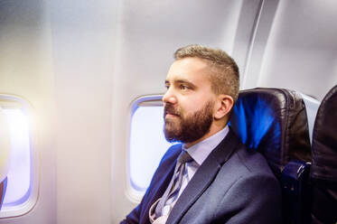 Young handsome businessman sitting inside an airplane - HPIF35752