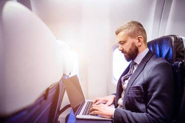 Junger gut aussehender Geschäftsmann mit Notebook in einem Flugzeug sitzend - HPIF35754