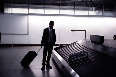 Silhouette eines Geschäftsmannes, der auf dem Gepäckband im Flughafen auf seinen Koffer wartet - HPIF35755