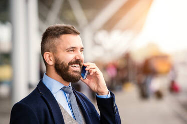 Hipster-Geschäftsmann im Anzug beim Telefonieren, Warten am Flughafen, sonniger Tag - HPIF35760