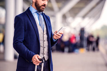 Hipster businessman in suit with smart phone, waiting at the airport, sunny day - HPIF35761